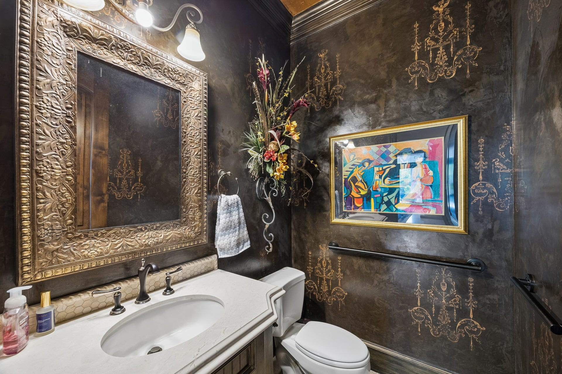 8111 Marshall Falls Drive, Spring, TX 77379 Luxurious powder room featuring elegant dark walls with gold accents, an ornate framed mirror, and vibrant artwork, creating a sophisticated ambiance. There are two powder rooms for added convenience.