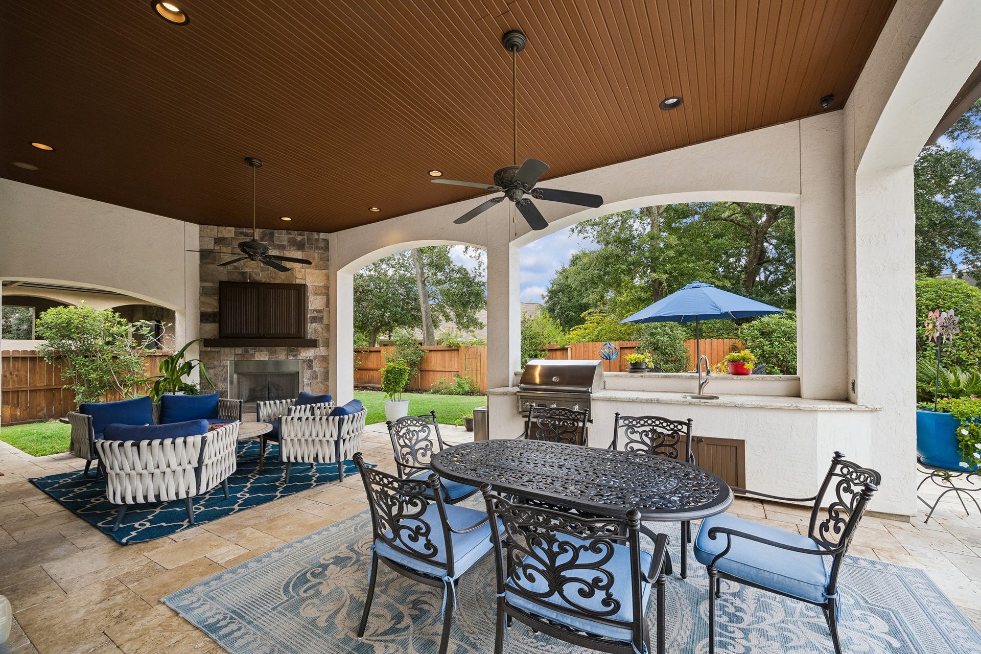 8111 Marshall Falls Drive, Spring, TX 77379 Luxurious outdoor living space featuring a covered patio with an outdoor TV, cozy seating around a fireplace, plus additional seating for outdoor dining, Viking built-in grill, and lush garden views.