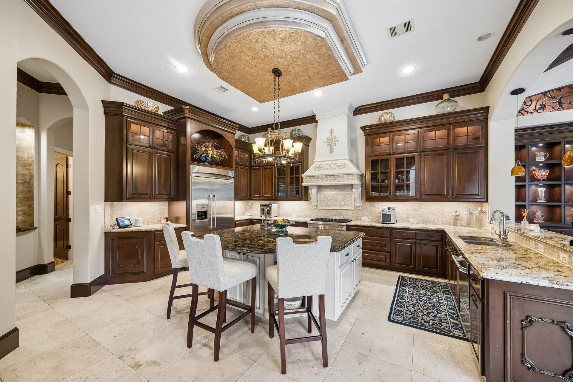8111 Marshall Falls Drive, Spring, TX 77379 Elegant kitchen featuring rich wooden cabinetry, a large central island with seating, and high-end stainless steel appliances including a built-in fridge/freezer, 6 burner gas range with professional vent hood, microwave, dishwasher and warming drawer all under a stunning coffered ceiling.