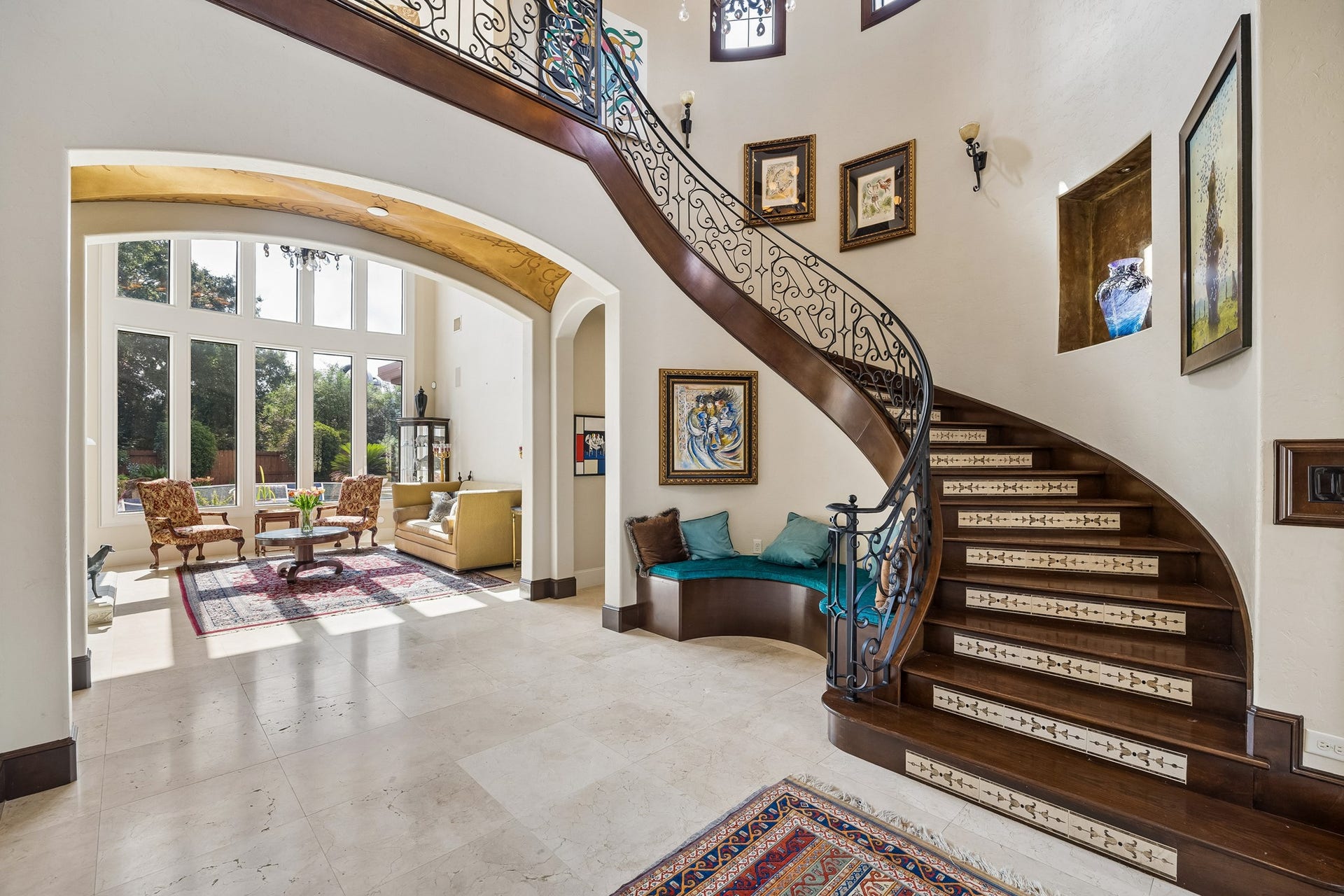 8111 Marshall Falls Drive, Spring, TX 77379 Grand foyer with a stunning curved staircase, ornate iron railing, and a cozy seating nook. Abundant natural light floods the adjacent living room, creating a welcoming atmosphere.