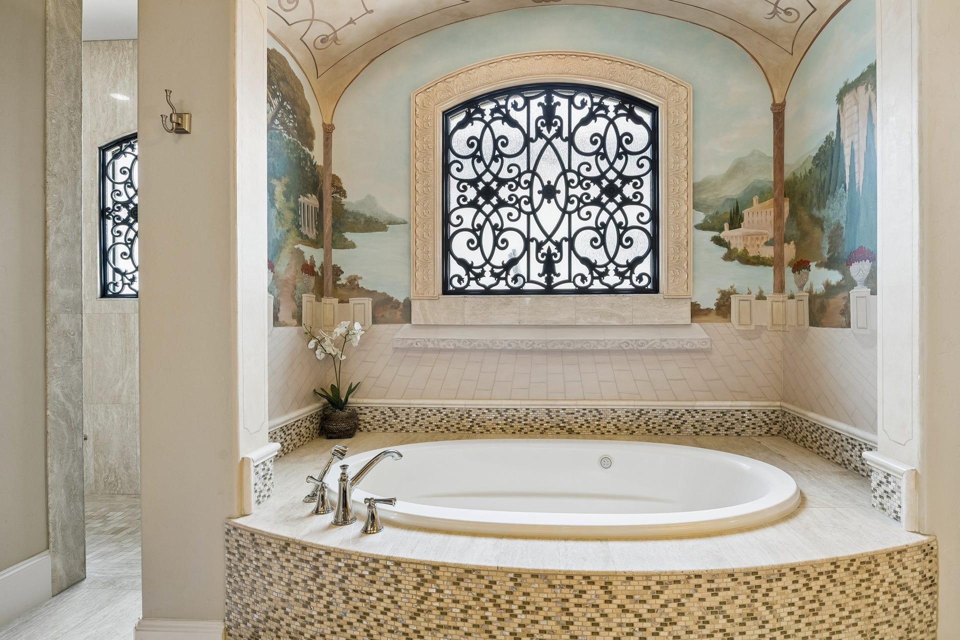 8111 Marshall Falls Drive, Spring, TX 77379 Luxurious bathroom featuring a stunning soaking tub with elegant mosaic tiling, set beneath a beautifully detailed mural and decorative arched window, creating a serene retreat.