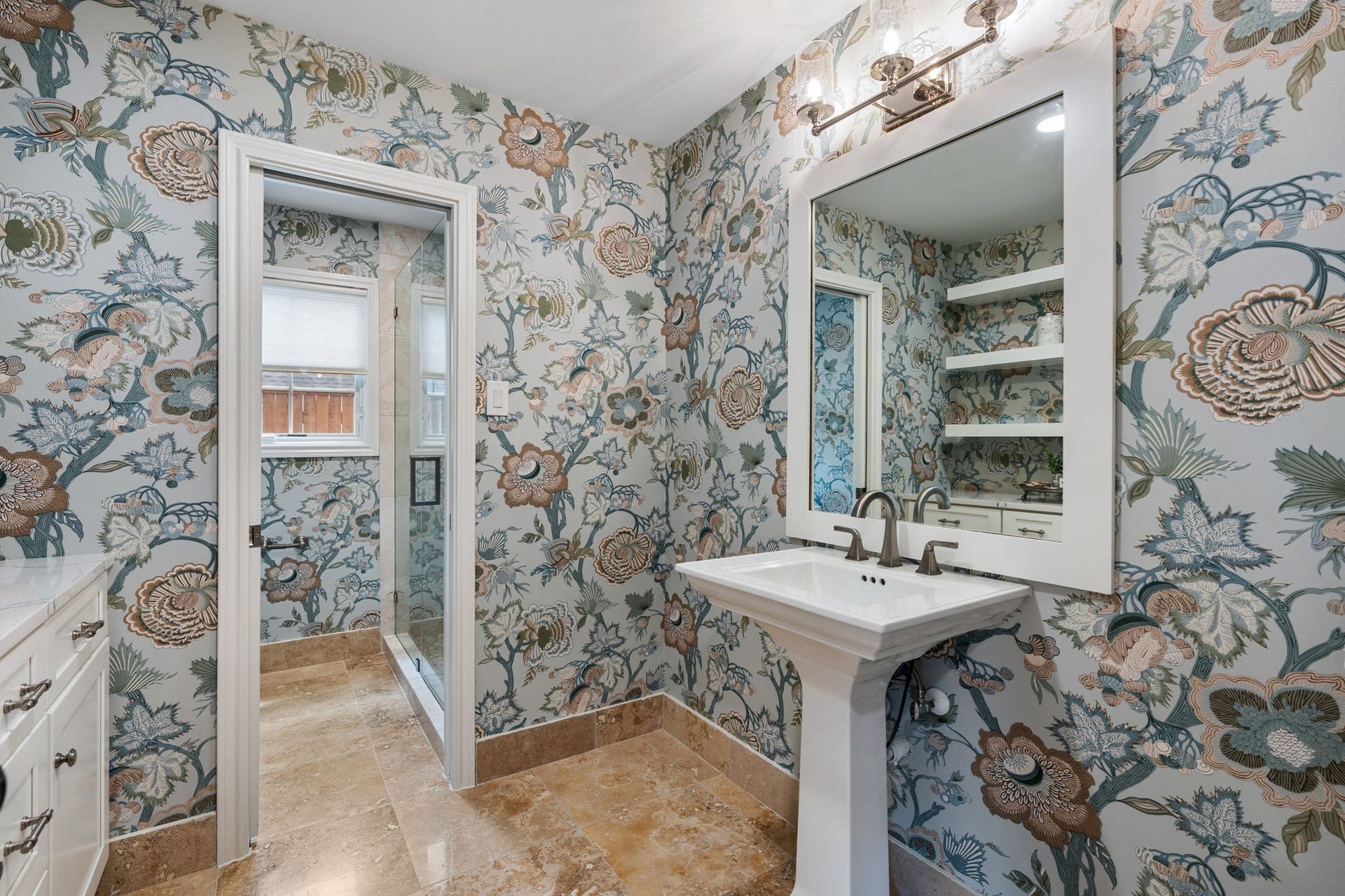 11407 Holidan Way, Hedwig Village, TX 77024 Beautifully remodeled full bath conveniently located just outside the first-floor secondary bedroom. Updated in 2025 w/ wallpaper added in 2026, the space features a pedestal sink, floating storage shelves & a separate room w/ shower & toilet for added functionality.