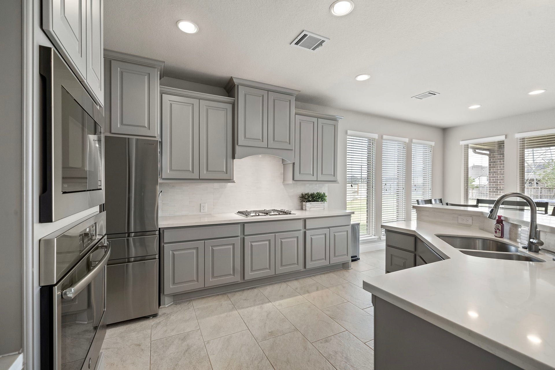 6902 N Elmwood Trail, Katy, TX 77493 Sleek and modern kitchen featuring gray cabinetry, stainless steel appliances, and an elegant island. Ample natural light streams through large windows, creating a bright and inviting space.