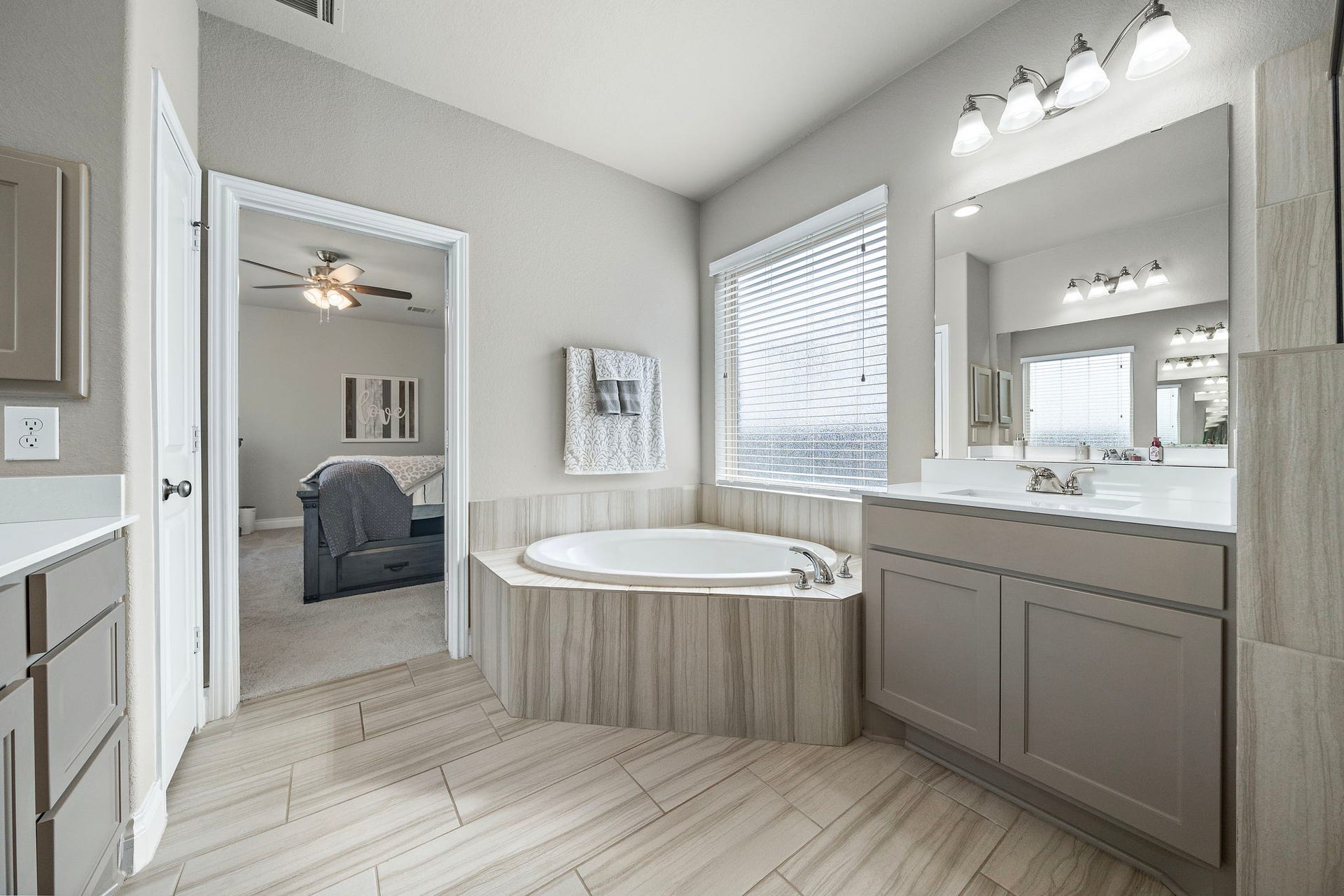 6902 N Elmwood Trail, Katy, TX 77493 Elegant bathroom featuring a luxurious corner soaking tub, dual vanity with modern fixtures, and a large window for natural light, seamlessly connected to a cozy bedroom.