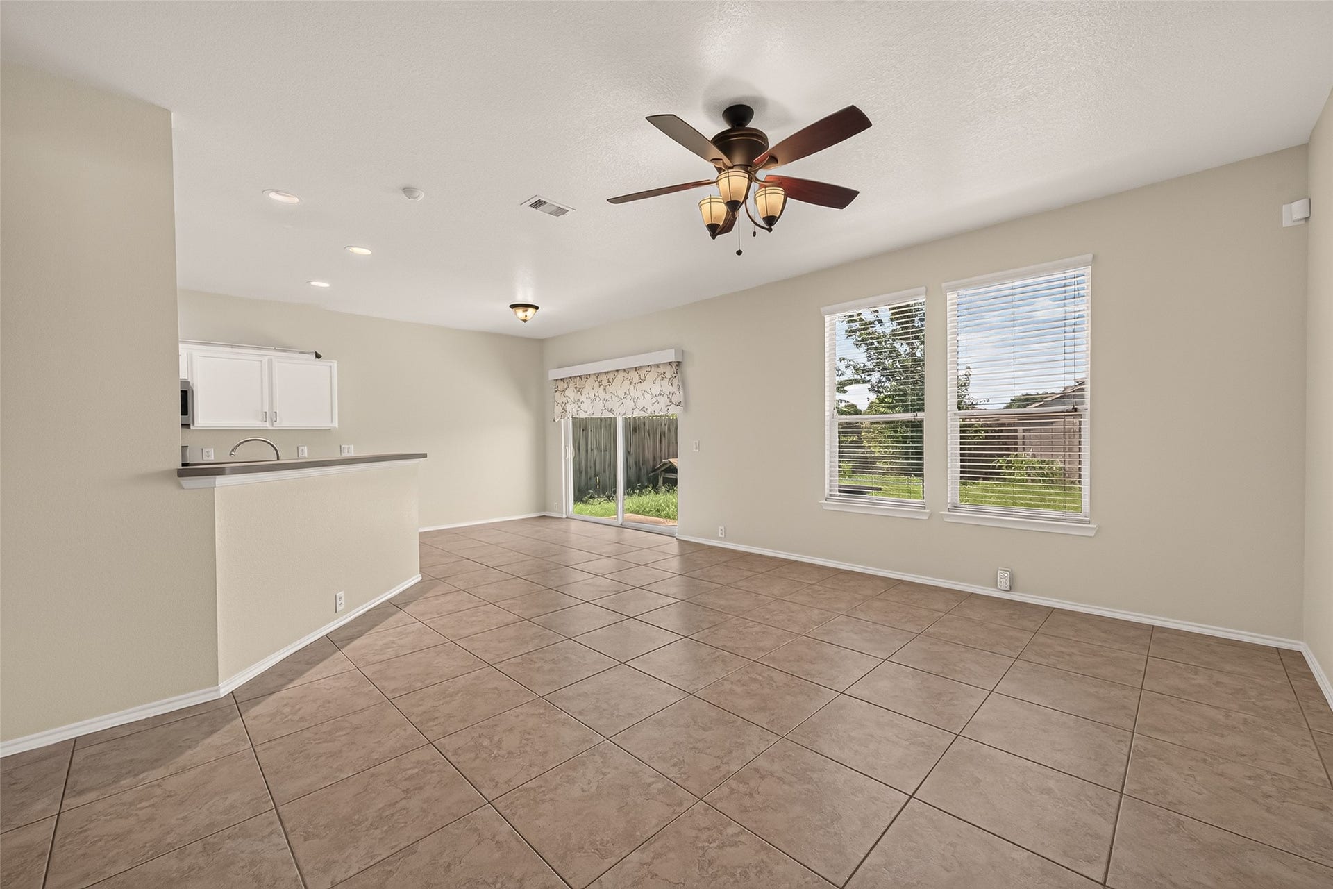 26130 Ripley Hills Drive, Richmond, TX 77406 Bright open living space with large windows, tiled flooring, and a ceiling fan. The room connects to a kitchen with a breakfast bar, and a sliding glass door leads to the backyard.