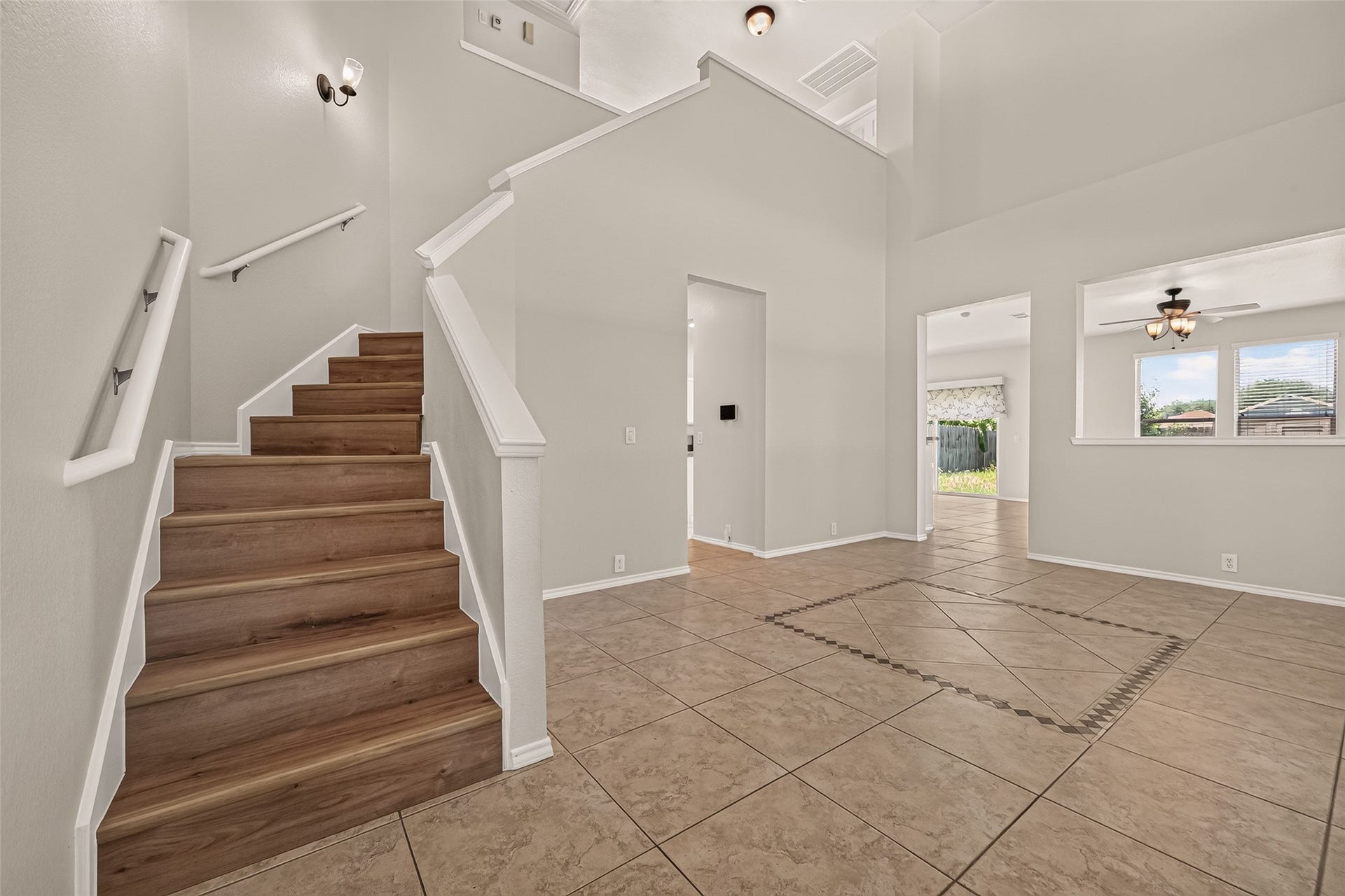 26130 Ripley Hills Drive, Richmond, TX 77406 This photo showcases a bright, open entryway with neutral walls and tiled flooring. A wooden staircase leads upstairs, and there are open doorways providing a view to additional rooms, including one with large windows and a ceiling fan. The space feels modern and welcoming.