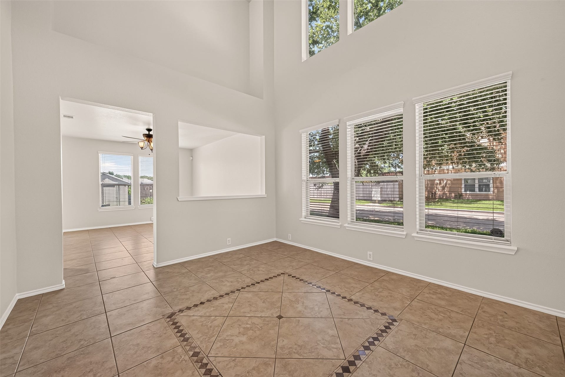 26130 Ripley Hills Drive, Richmond, TX 77406 This spacious room features high ceilings and large windows that let in plenty of natural light. The tile flooring includes a decorative inlay, and there's an open view into an adjacent room with a ceiling fan.