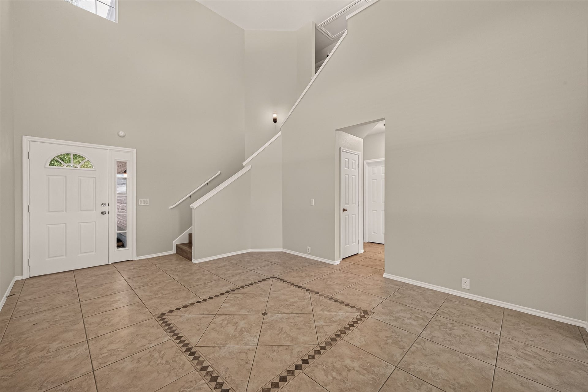 26130 Ripley Hills Drive, Richmond, TX 77406 This photo showcases a spacious, light-filled entryway with high ceilings and elegant tile flooring. It features a staircase leading to the upper level and a doorway to an adjacent room, offering a welcoming and open feel.