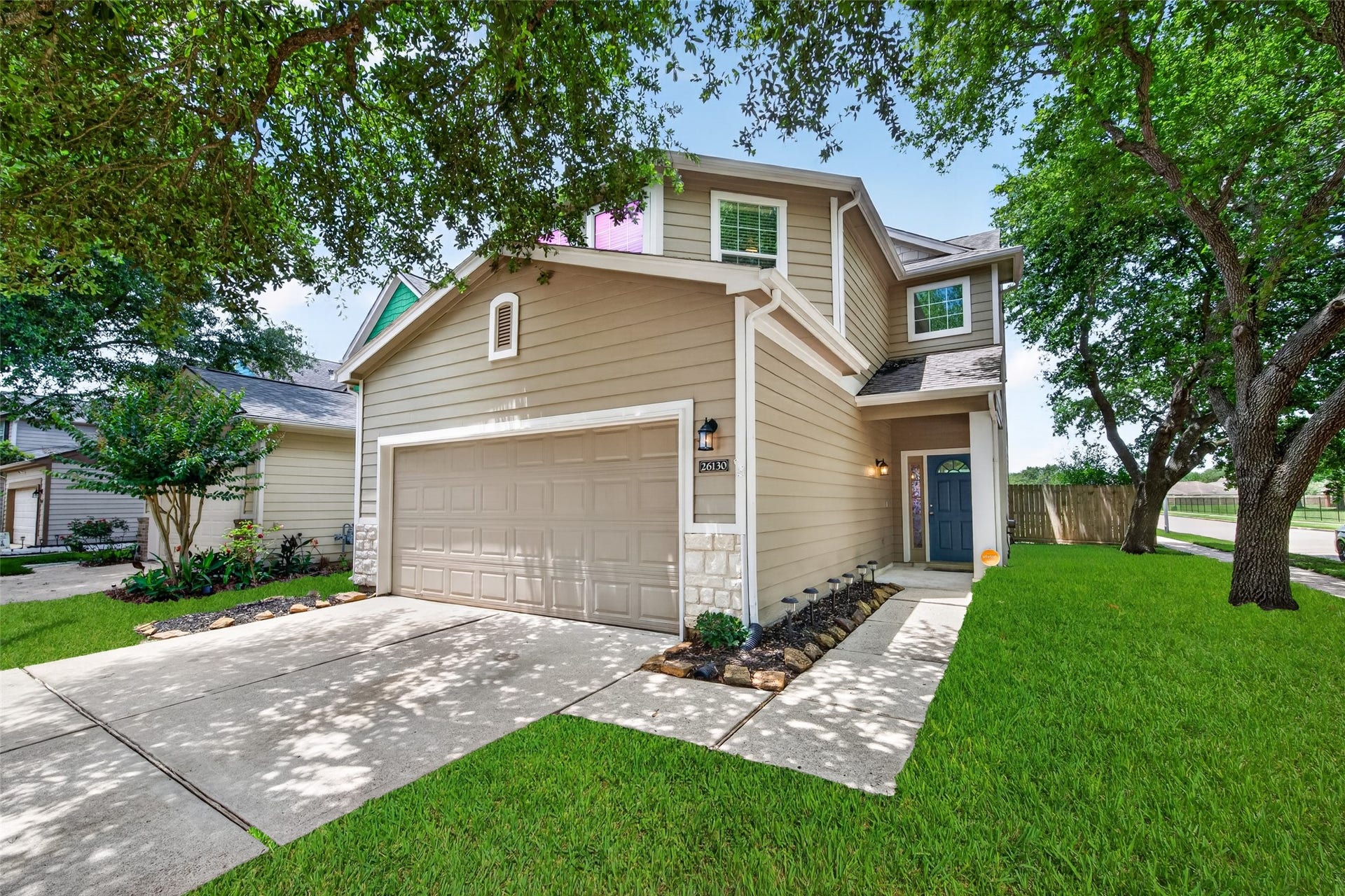 26130 Ripley Hills Drive, Richmond, TX 77406 This charming two-story home features a beige exterior with stone accents, a two-car garage, and a welcoming front entrance. It's surrounded by lush green lawns and mature trees, providing a serene and inviting atmosphere.