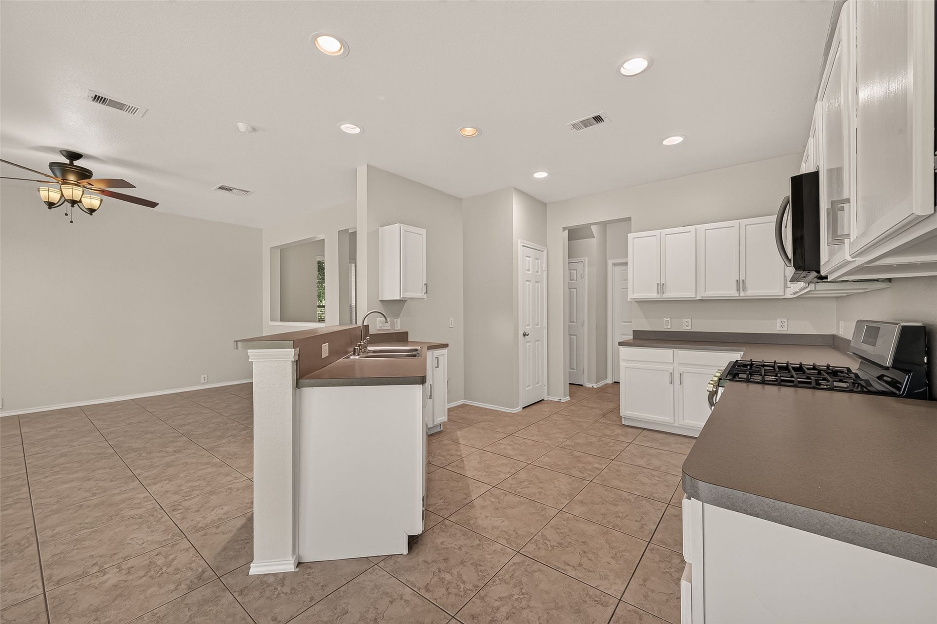 26130 Ripley Hills Drive, Richmond, TX 77406 This photo showcases a spacious kitchen with modern appliances, white cabinetry, and a brown countertop. The open layout extends into a living area with tiled flooring and a ceiling fan, creating an inviting space perfect for entertaining.