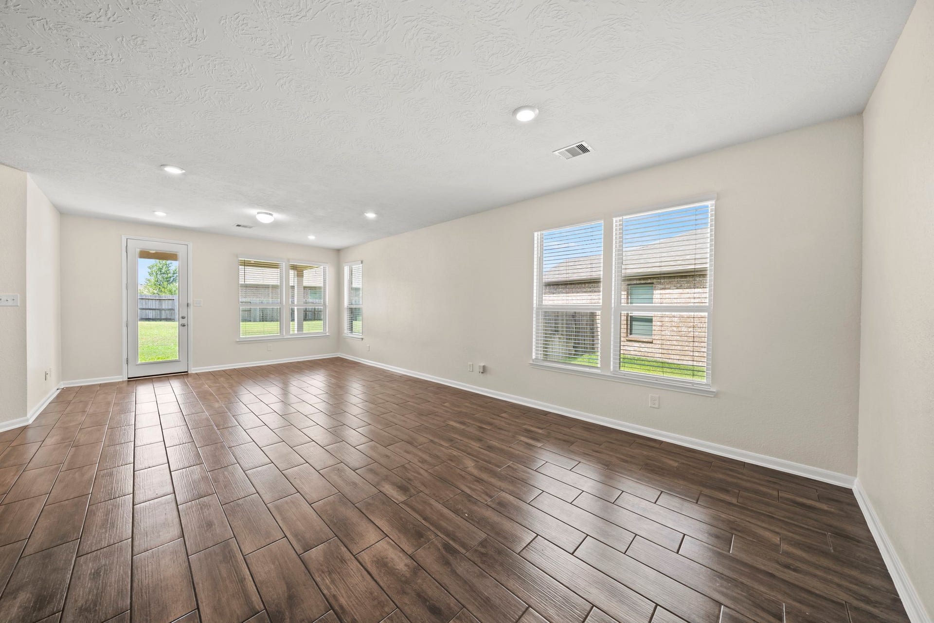 8908 Bear Mountain Court, Magnolia, TX 77354 Spacious main living area featuring rich wood-look tile flooring. Flooded with natural light from large windows, this open layout offers seamless connectivity to the backyard patio.