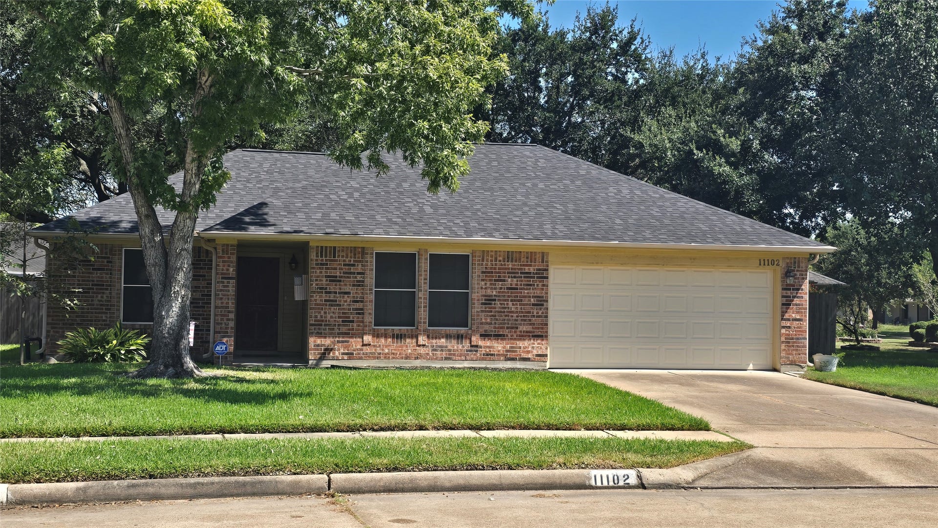 Charming brick home with a welcoming front yard, mature trees, and a spacious two-car garage.