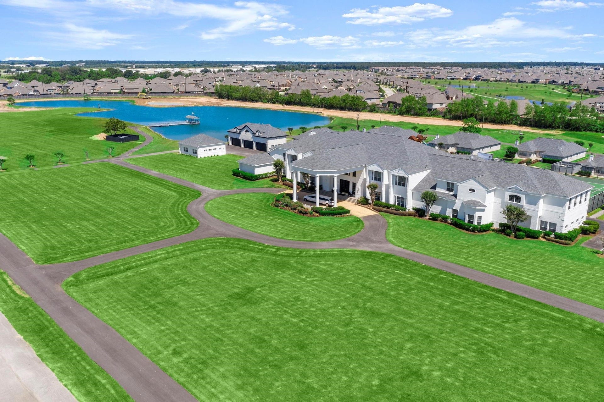 This aerial photo showcases a spacious, modern residential community with beautifully manicured lawns, a sizable body of water providing scenic waterfront views, and a variety of contemporary homes with ample yard space. The neighborhood is well-planned with winding roads and appears to offer a tranquil suburban lifestyle.