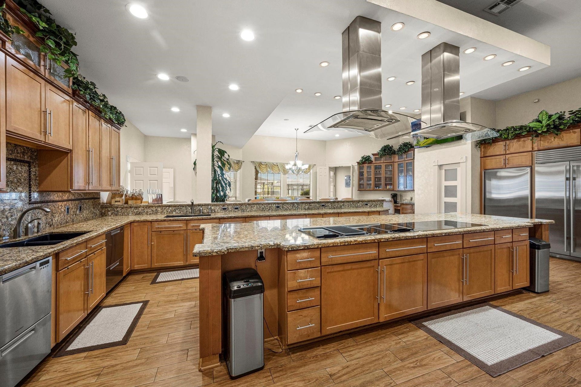 This spacious kitchen features modern stainless steel appliances, ample wooden cabinetry, granite countertops, and a large island. It's well-lit with a combination of recessed and pendant lighting, and offers an open layout with a view into the adjoining living spaces.