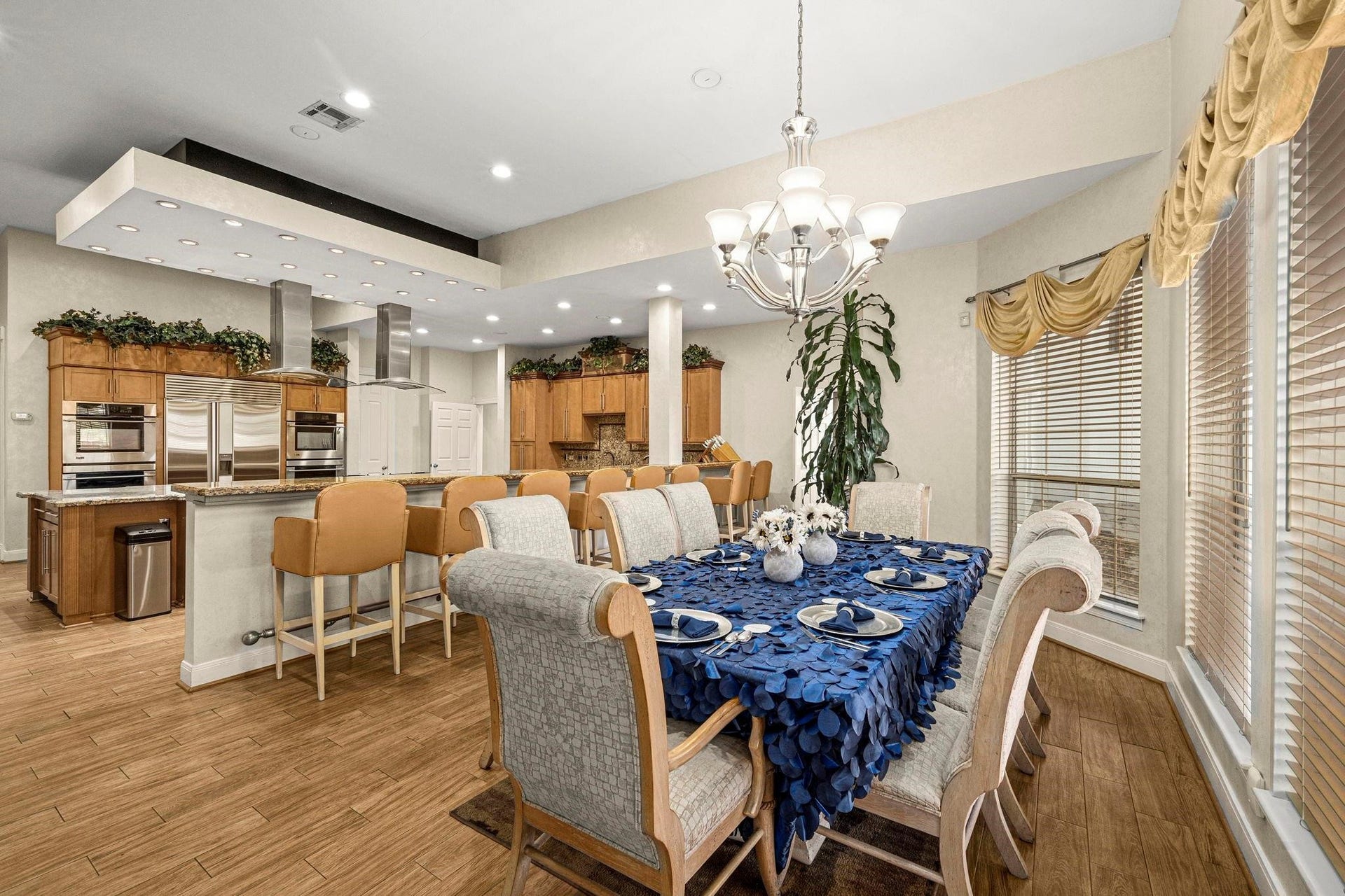 This photo showcases a spacious, open-concept dining and kitchen area with modern appliances, ample cabinetry, and elegant lighting. The breakfast space features a large table set for entertaining, complemented by a sophisticated chandelier. The room is well-lit and inviting, with a warm color palette and hardwood flooring.