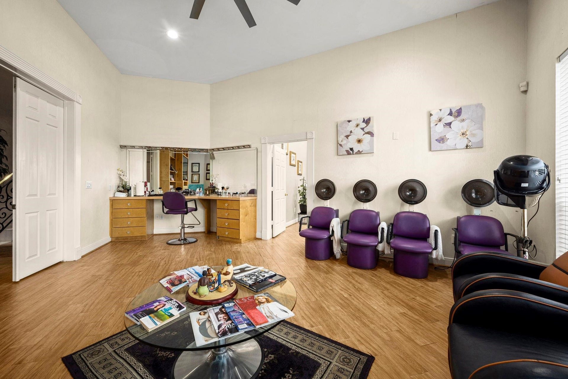 This room is currently set up as a hair salon with multiple styling chairs, hair washing stations, and a hair dryer station. It features wood flooring, a high ceiling with a fan, and is well-lit. The space could be easily converted to suit various other purposes depending on your needs.