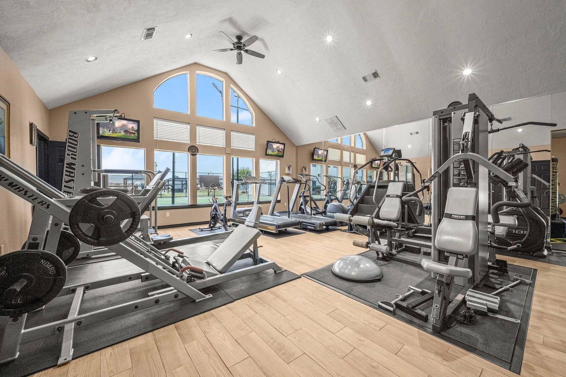 This is a spacious Fitness Center, with high ceilings, large arched windows providing natural light, and a variety of fitness equipment, perfect for a fitness enthusiast looking for a private workout space.