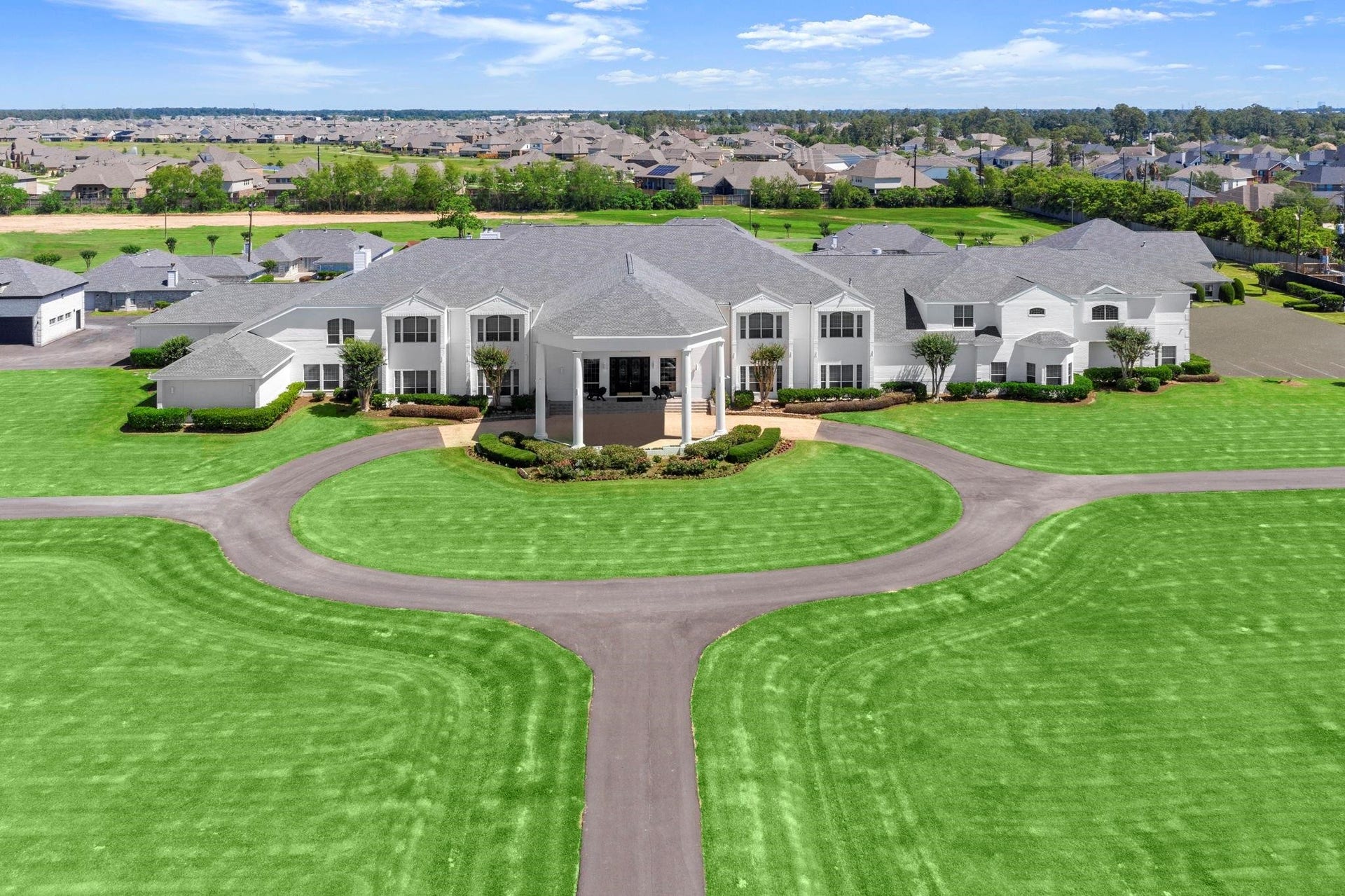 This is an aerial view of a spacious 2 story home with a symmetric facade, well-manicured lawns, and a circular driveway, set in a suburban style neighborhood with similar upscale houses.