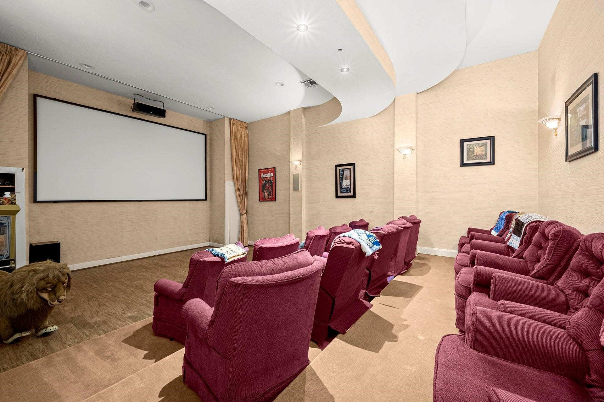 This is a cozy home theater room featuring comfortable tiered seating, a large screen for an immersive viewing experience, and elegant lighting for the perfect movie night ambiance.
