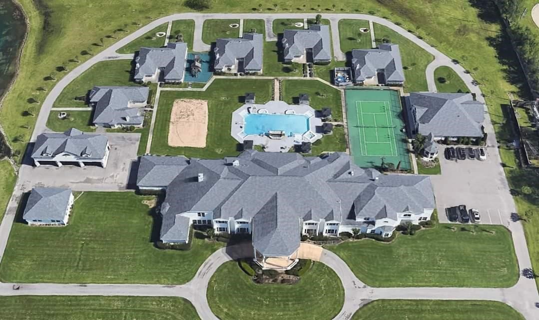 This aerial photo showcases a luxurious residential area with spacious, detached homes, featuring well-maintained lawns and amenities such as a swimming pool and a tennis court, indicating a high-end, community-oriented neighborhood.