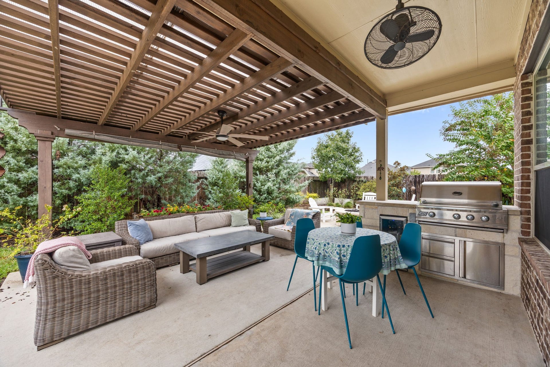Charming outdoor patio featuring a pergola, cozy seating, dining area, and a built-in grill, perfect for entertaining and relaxation amidst lush greenery.