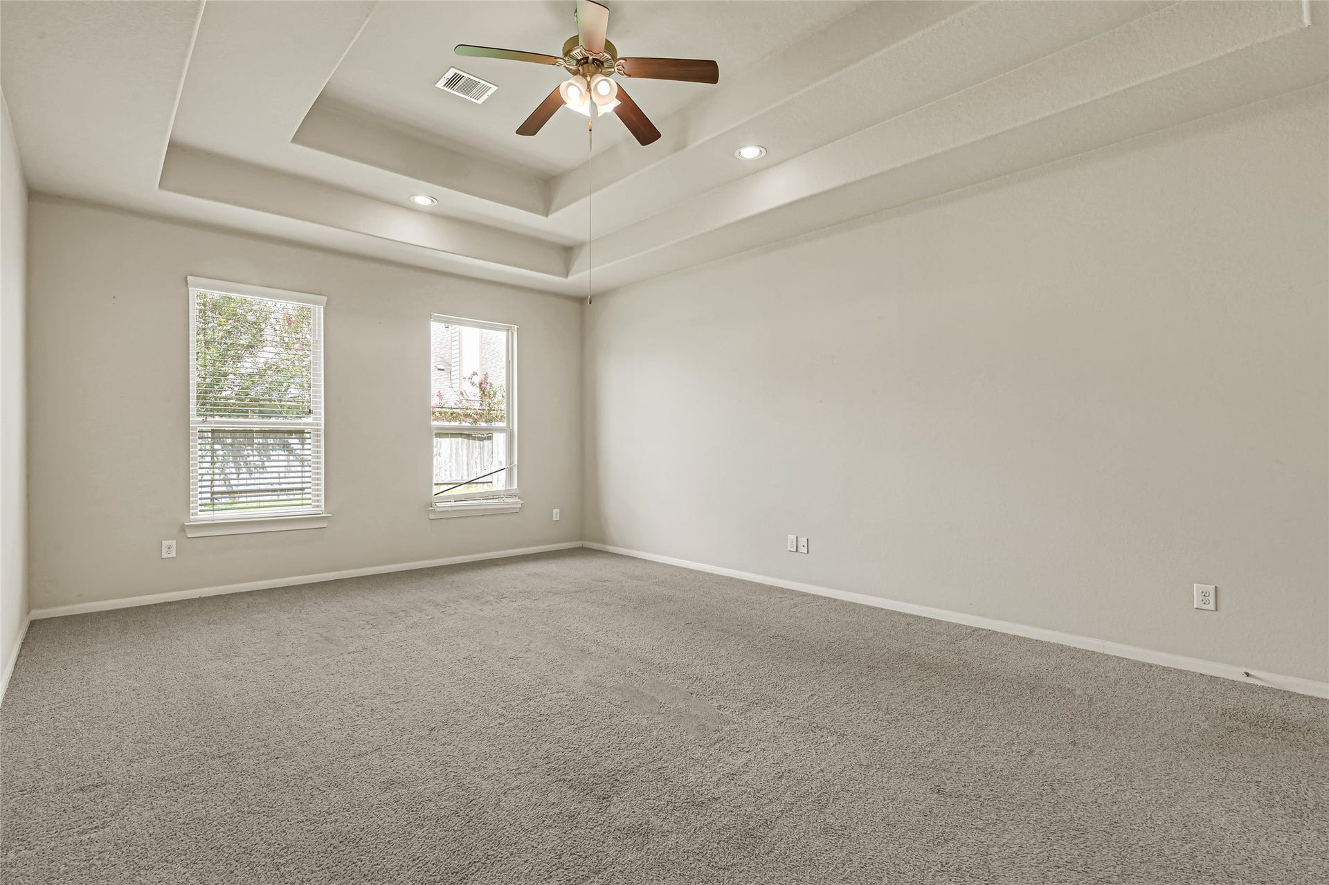 736 Somerset Landing Lane, League City, TX 77573 Large bedroom with ceiling fan, tray ceiling, multiple windows, and neutral carpet.