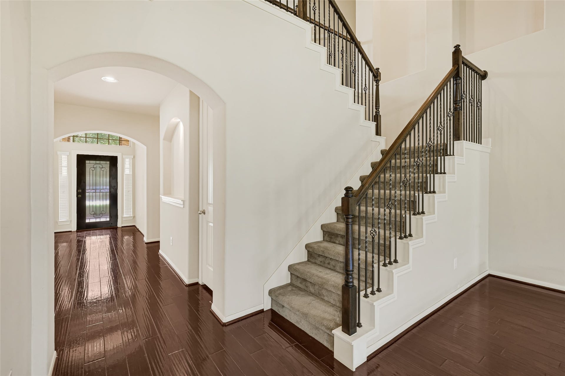 736 Somerset Landing Lane, League City, TX 77573 Open staircase with wrought-iron railing, hardwood flooring, and arched interior openings.