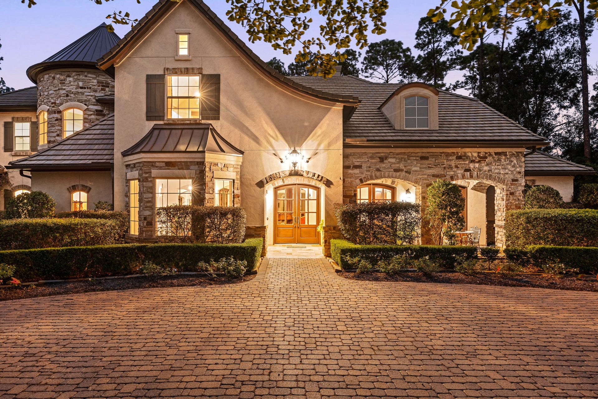 2127 Fawn Meadow Lane, Richmond, TX 77406 Gorgeous evening view highlighting the home's elegant French country exterior, pave stone circle driveway, and warm lighting off the front porch.