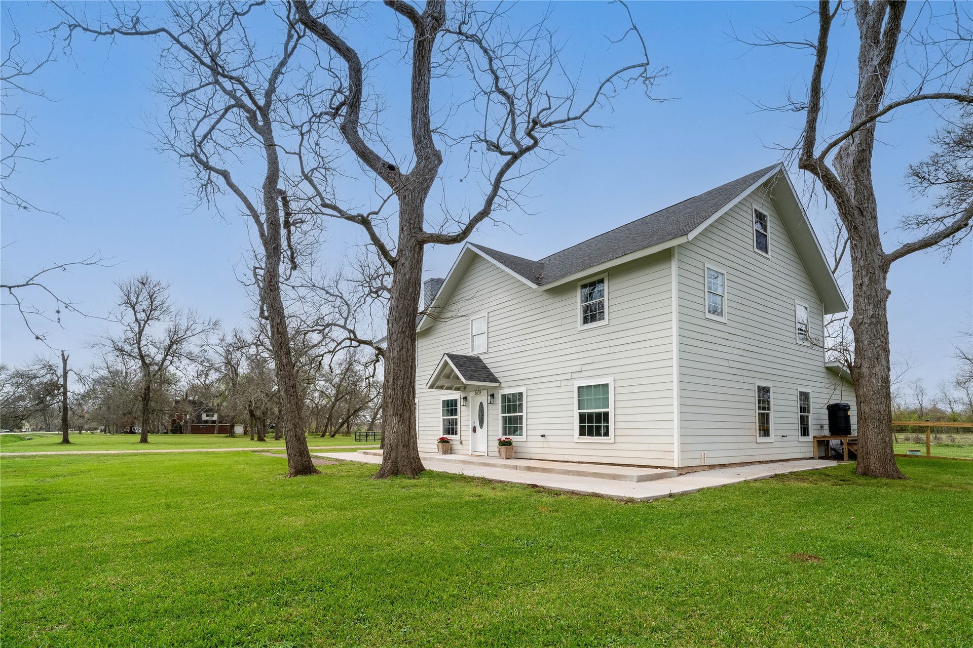 1635 Pony Lane, Wallis, TX 77485 Front Exterior Angle Side perspective of the home highlighting the expansive property, mature trees, and spacious country setting.