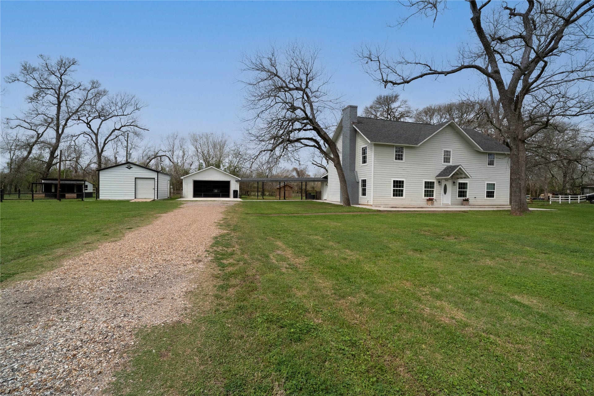 1635 Pony Lane, Wallis, TX 77485 Front Exterior / Property View Scenic approach to the home with a long gravel driveway, mature pecan trees, and multiple outbuildings offering additional storage or workspace.