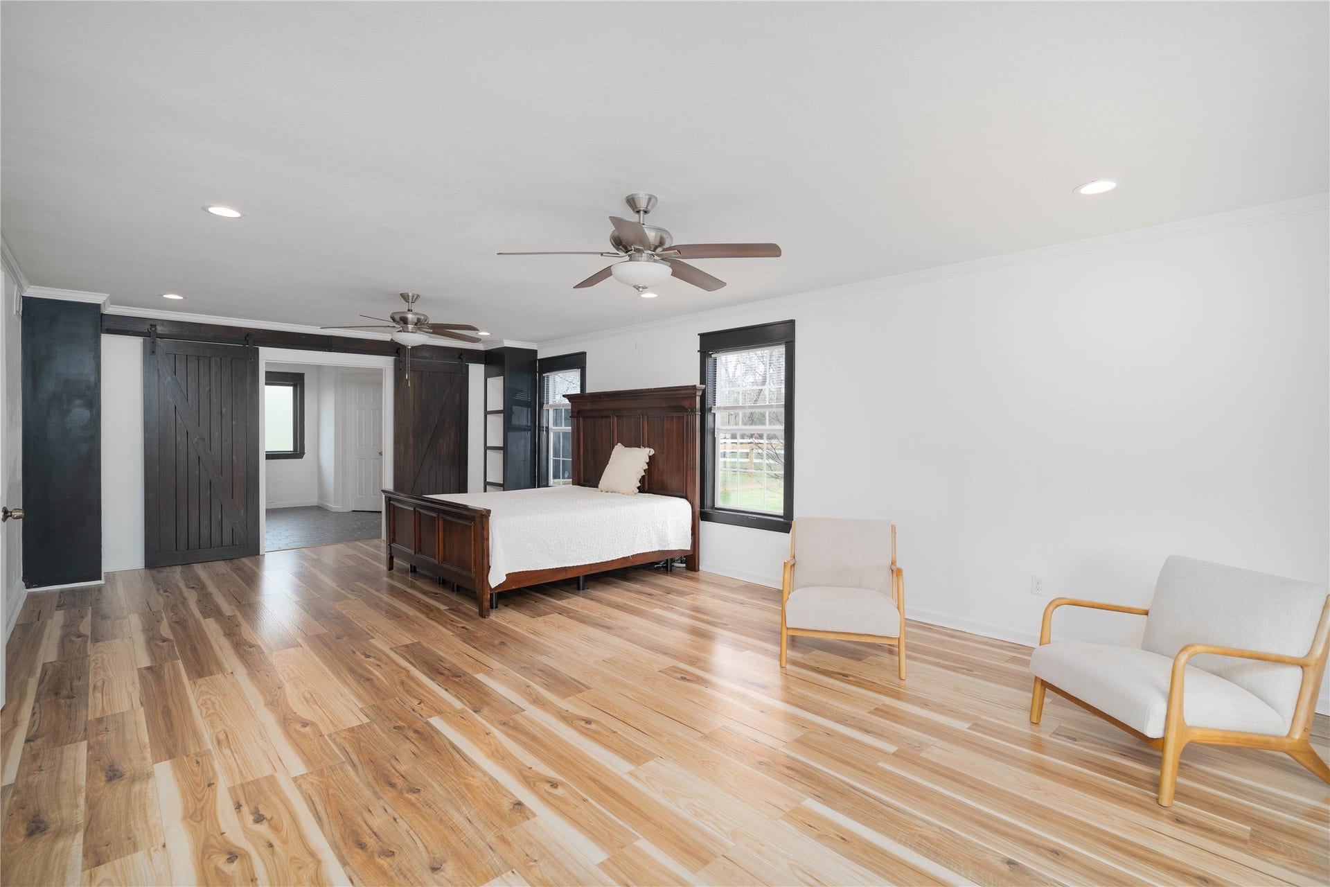 1635 Pony Lane, Wallis, TX 77485 Primary Bedroom Suite Expansive primary suite with wood-like flooring, abundant natural light, and custom sliding barn doors leading to the en-suite bath. Large seating area is ideal for relaxation and transition.