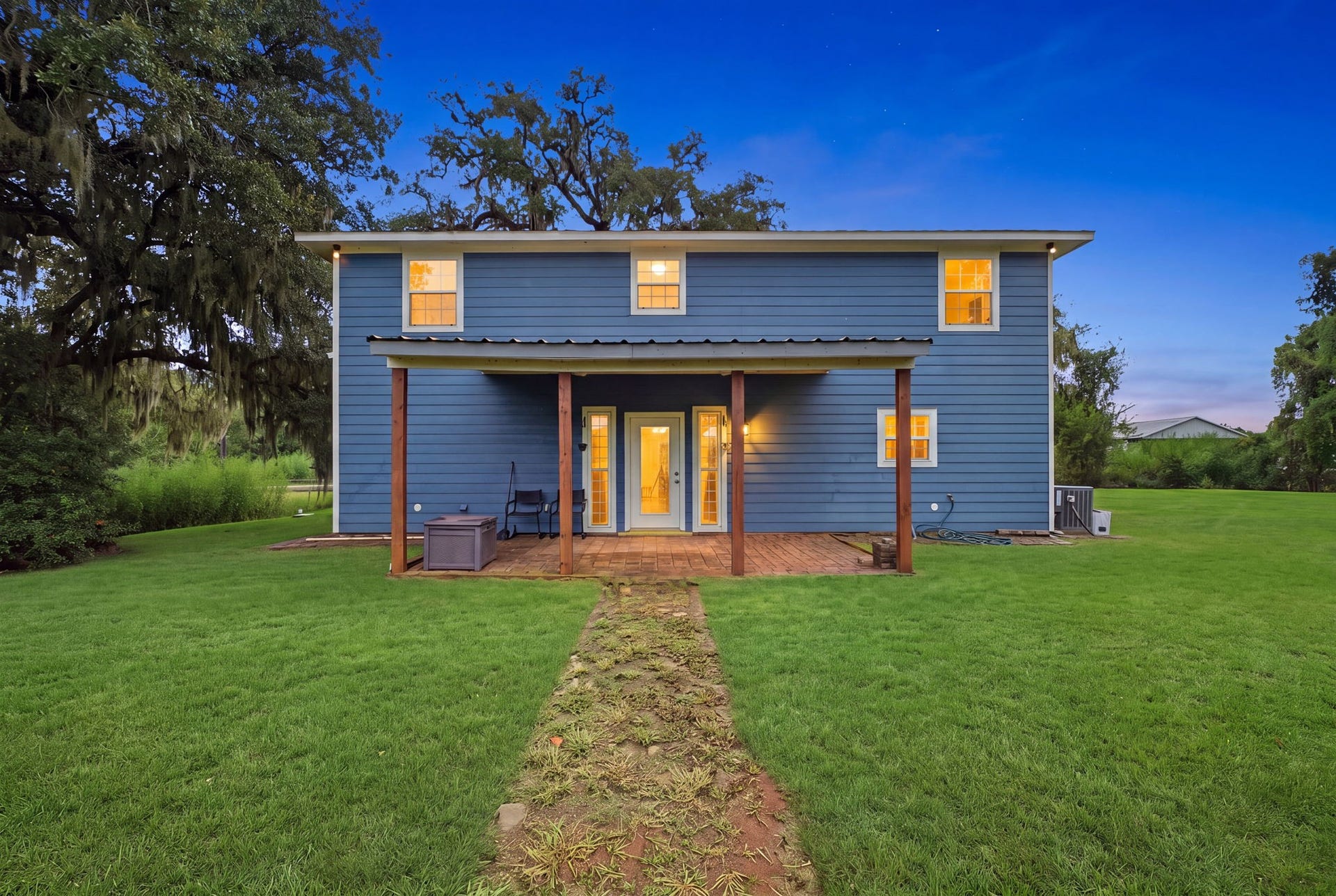 450 N Sunset Boulevard, Holiday Lakes, TX 77515 Rear Exterior: Mature oaks frame this glowing backyard retreat. A covered brick-paver patio overlooks a big, open lawn with plenty of room for a playground, play area, or backyard barbecues.