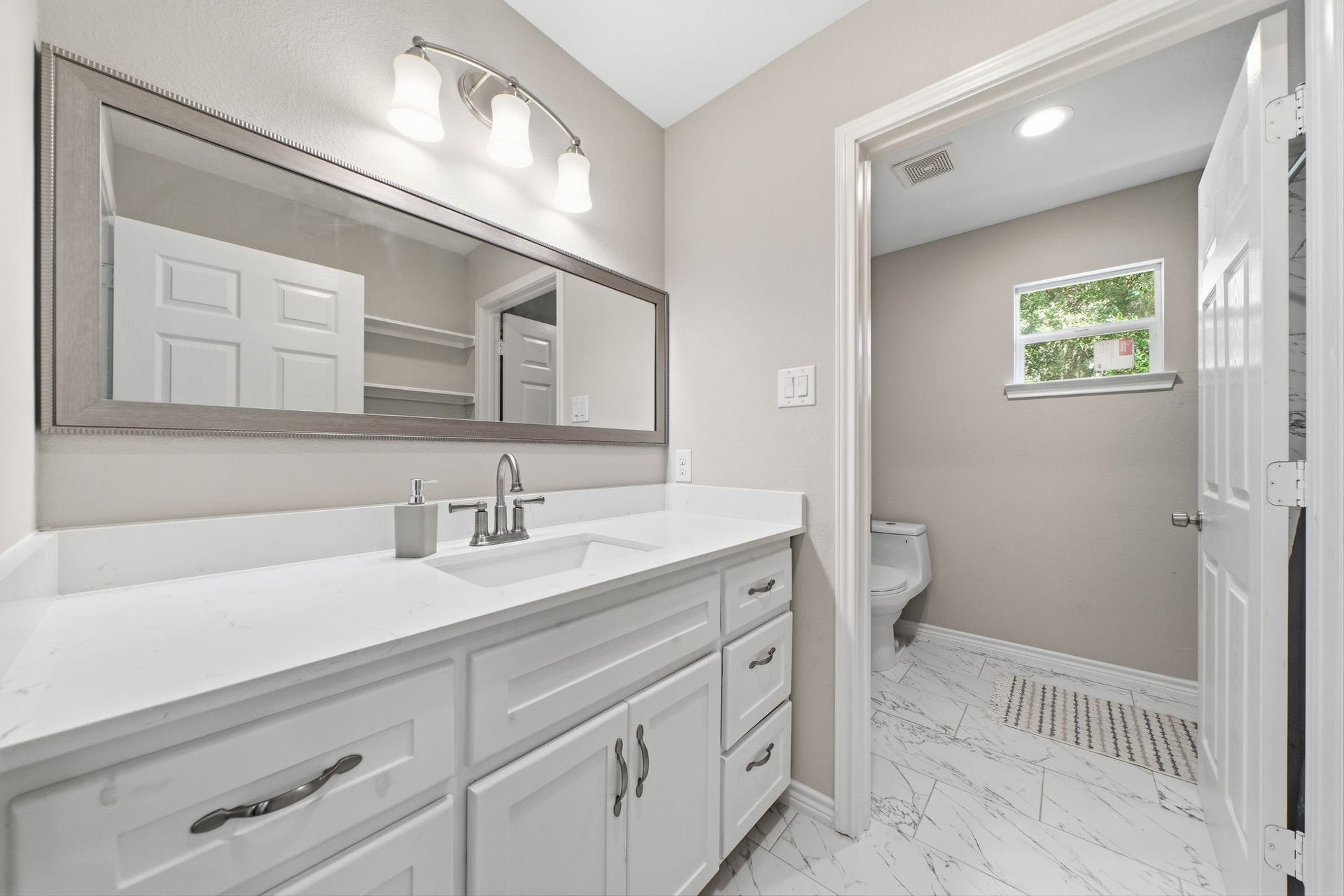 450 N Sunset Boulevard, Holiday Lakes, TX 77515 Vanity and Private Toilet Room: A long quartz vanity with plenty of drawer and cabinet storage makes busy mornings easier. A separate toilet room with a window and marble-look tile flooring adds privacy, and the walk-in closet is just steps away.