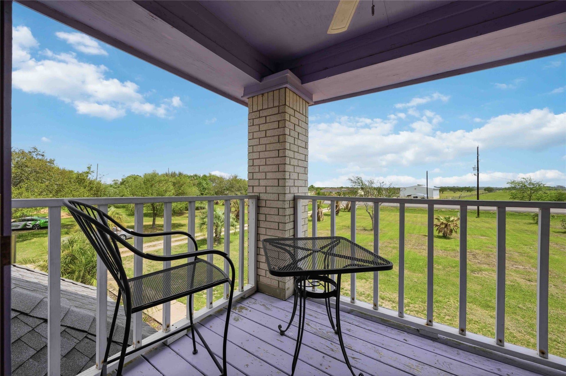 12075 FM 359 Road, #1, Hempstead, TX 77445 Cozy balcony with a small table and chairs, offering a relaxing view of a spacious, green lawn and trees. Ideal for enjoying the outdoors and peaceful surroundings.