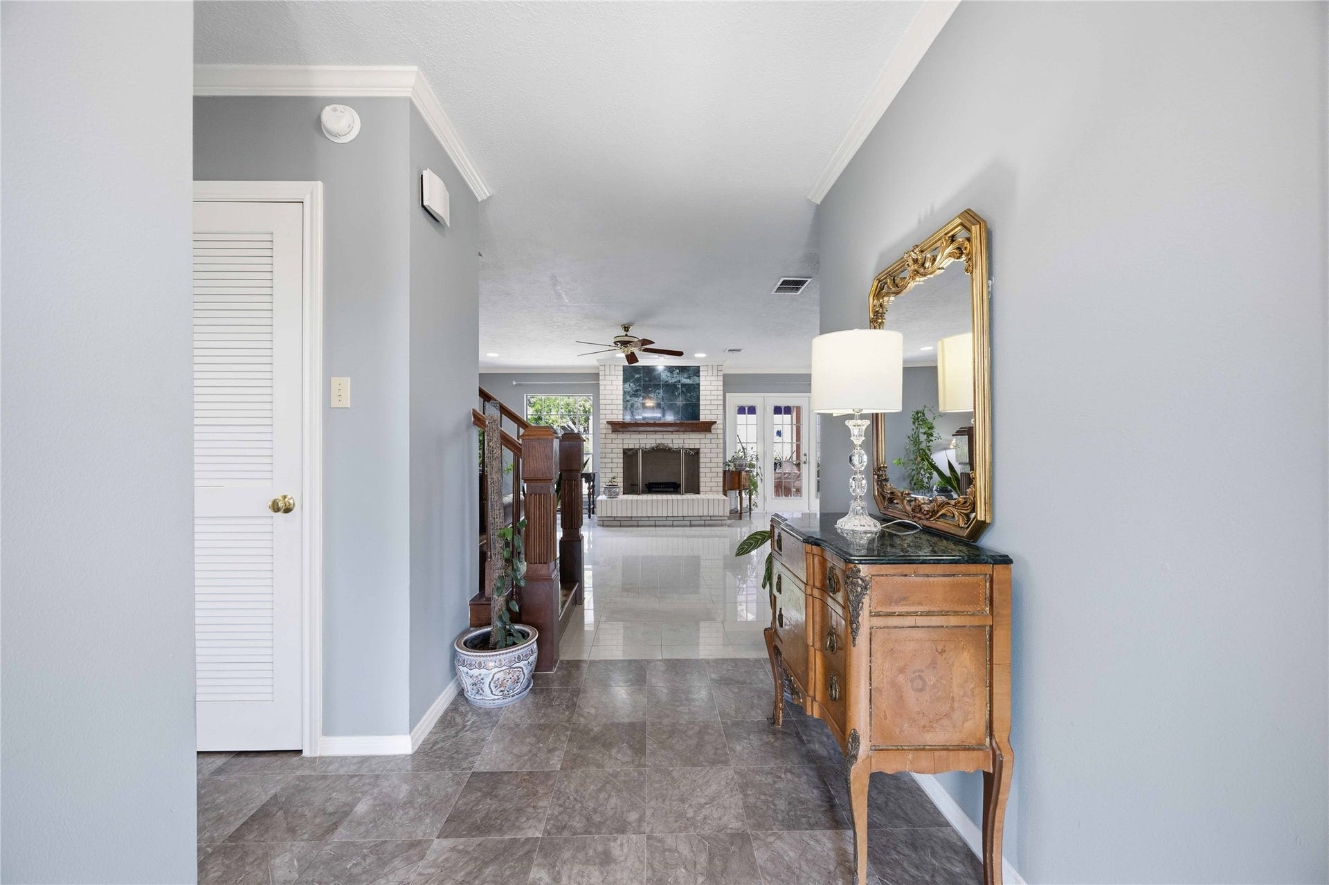 12075 FM 359 Road, #1, Hempstead, TX 77445 A welcoming entryway with elegant tile flooring leads to a bright living area featuring a cozy fireplace. A decorative mirror and vintage table add charm, while neutral walls enhance the spacious feel.