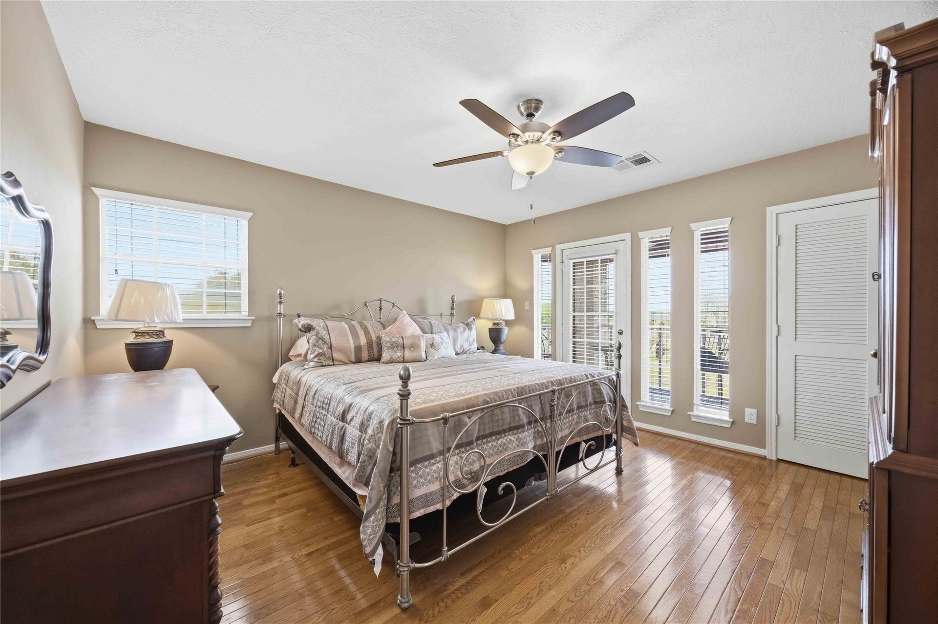12075 FM 359 Road, #1, Hempstead, TX 77445 Spacious and bright bedroom with green walls, featuring a ceiling fan, large bed, mounted TV, and ample natural light from multiple windows. A desk and dressers provide functional storage.