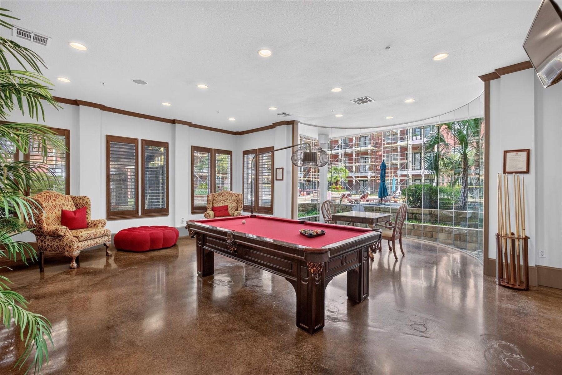 Residents have access to the game room featuring a classic billiard table, cozy seating with plush armchairs, and expansive windows offering a view of the lush outdoor courtyard.