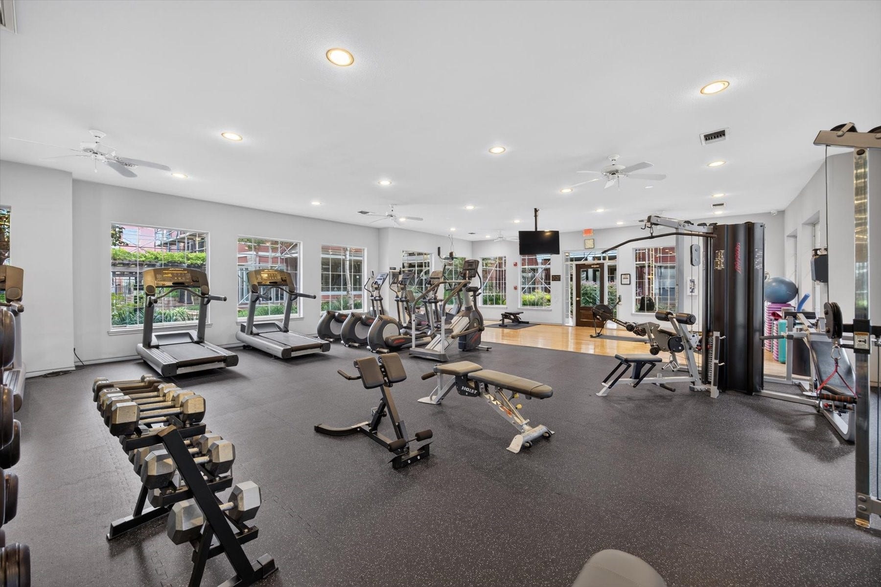 Building offers a fitness center equipped with modern cardio machines, free weights, and strength training equipment, surrounded by large windows for natural light.
