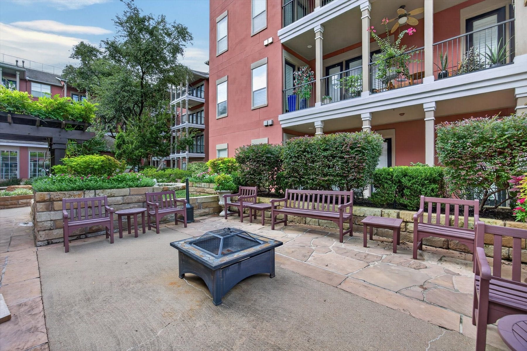 Discover a charming outdoor courtyard perfect for relaxation, featuring ample seating, lush greenery, and a central fire pit for cozy gatherings.