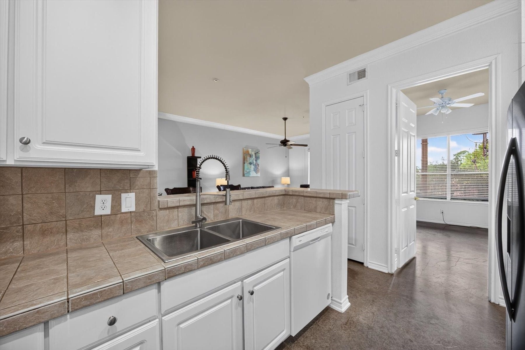 Bright kitchen with open view into the living area, leading to a sunlit room with large windows.