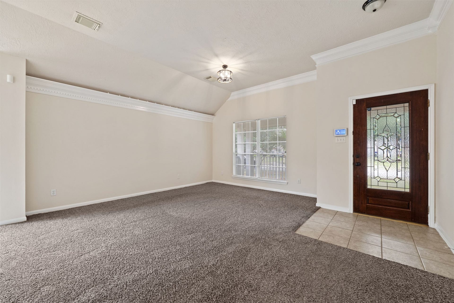 10902 Trail Ridge Drive, Houston, TX 77064 Focus on the living area with plush carpeting, elegant crown molding, and abundant natural light through a large window, complemented by a stylish wooden entry door with decorative glass.