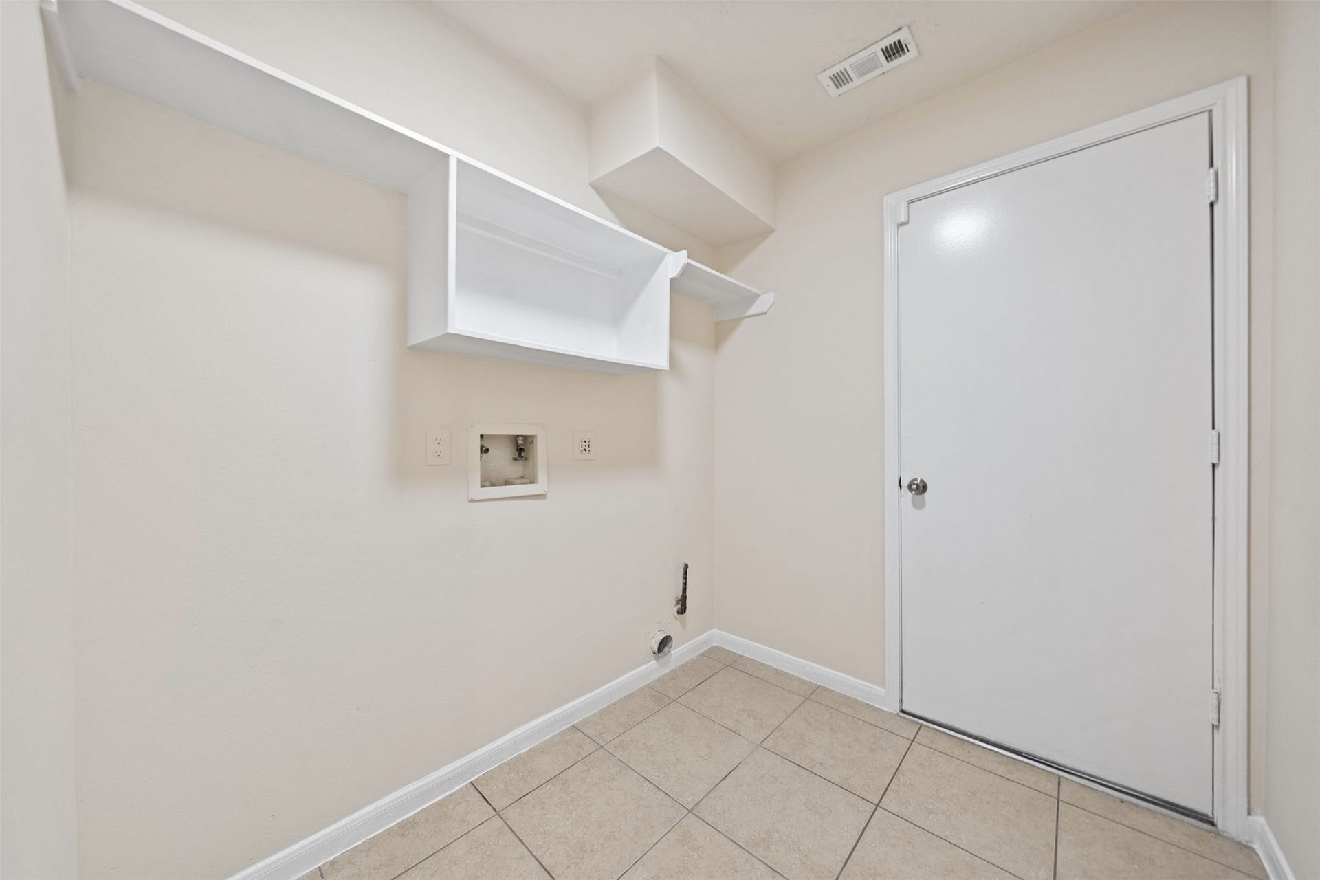 10902 Trail Ridge Drive, Houston, TX 77064 Laundry room with tiled floors, wall shelving, and hookups for a washer and dryer, providing functionality and storage.