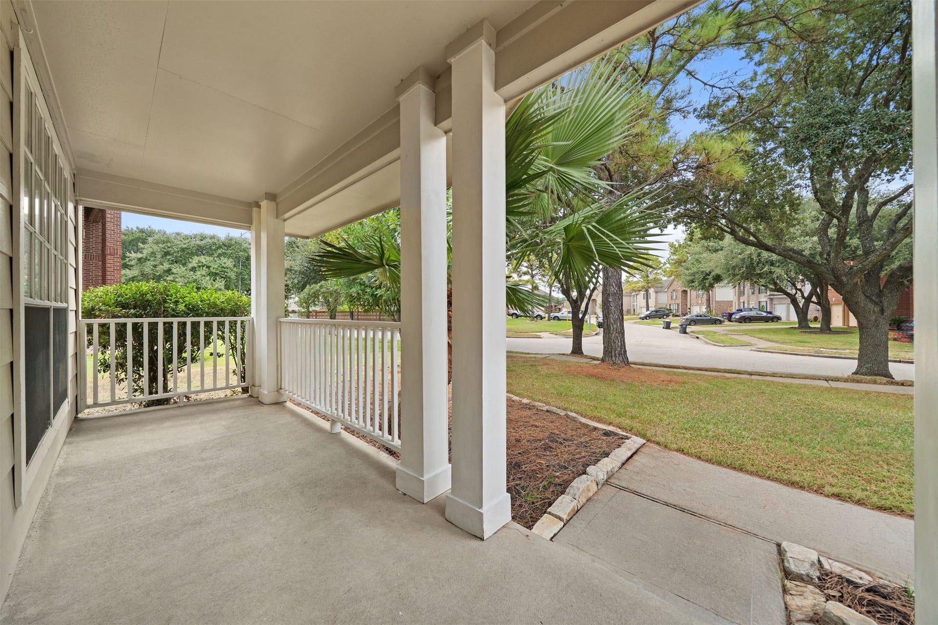 10902 Trail Ridge Drive, Houston, TX 77064 Charming front porch with classic railing overlooks a serene neighborhood street, surrounded by lush greenery and mature trees.