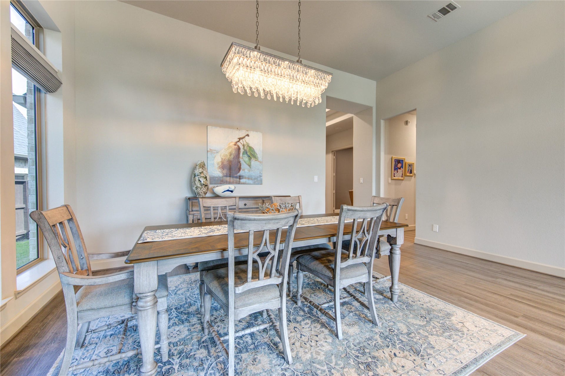 The formal dining room is a sophisticated space designed for gatherings and celebrations. Featuring high ceilings and wood plank luxury vinyl floors, this room exudes warmth and elegance. A large window allows natural light to pour in, creating a bright and inviting atmosphere.