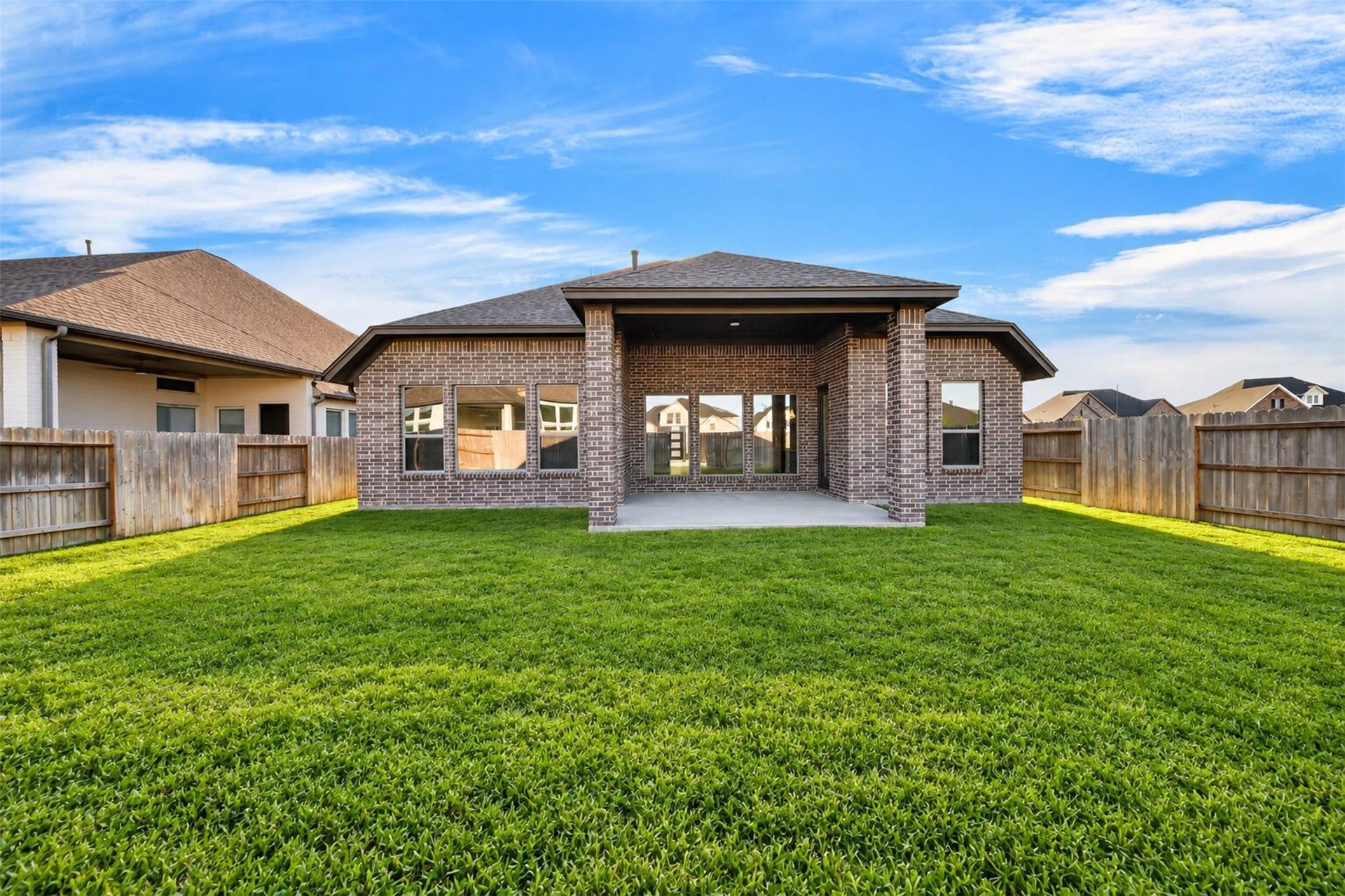 16270 Blue Mistflower Lane, Hockley, TX 77447 Rear Exterior & Covered Patio: Beautiful brick exterior overlooking a spacious, fully fenced backyard with lush green lawn and a generous covered patio designed for outdoor living and entertaining.