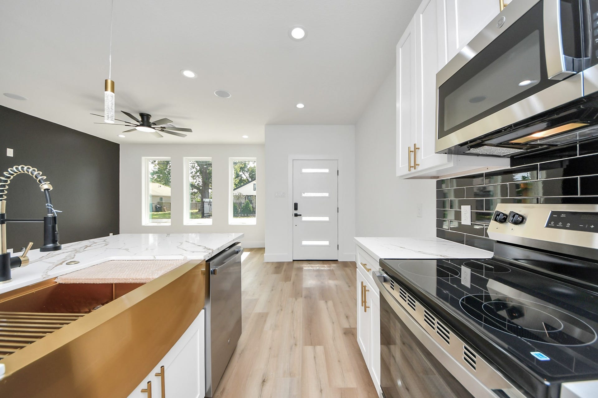 7801 King Street, Houston, TX 77028 Modern kitchen with sleek stainless steel appliances, elegant black backsplash, and a stylish gold-accented sink, seamlessly flowing into a bright living area with large windows and contemporary ceiling fan.