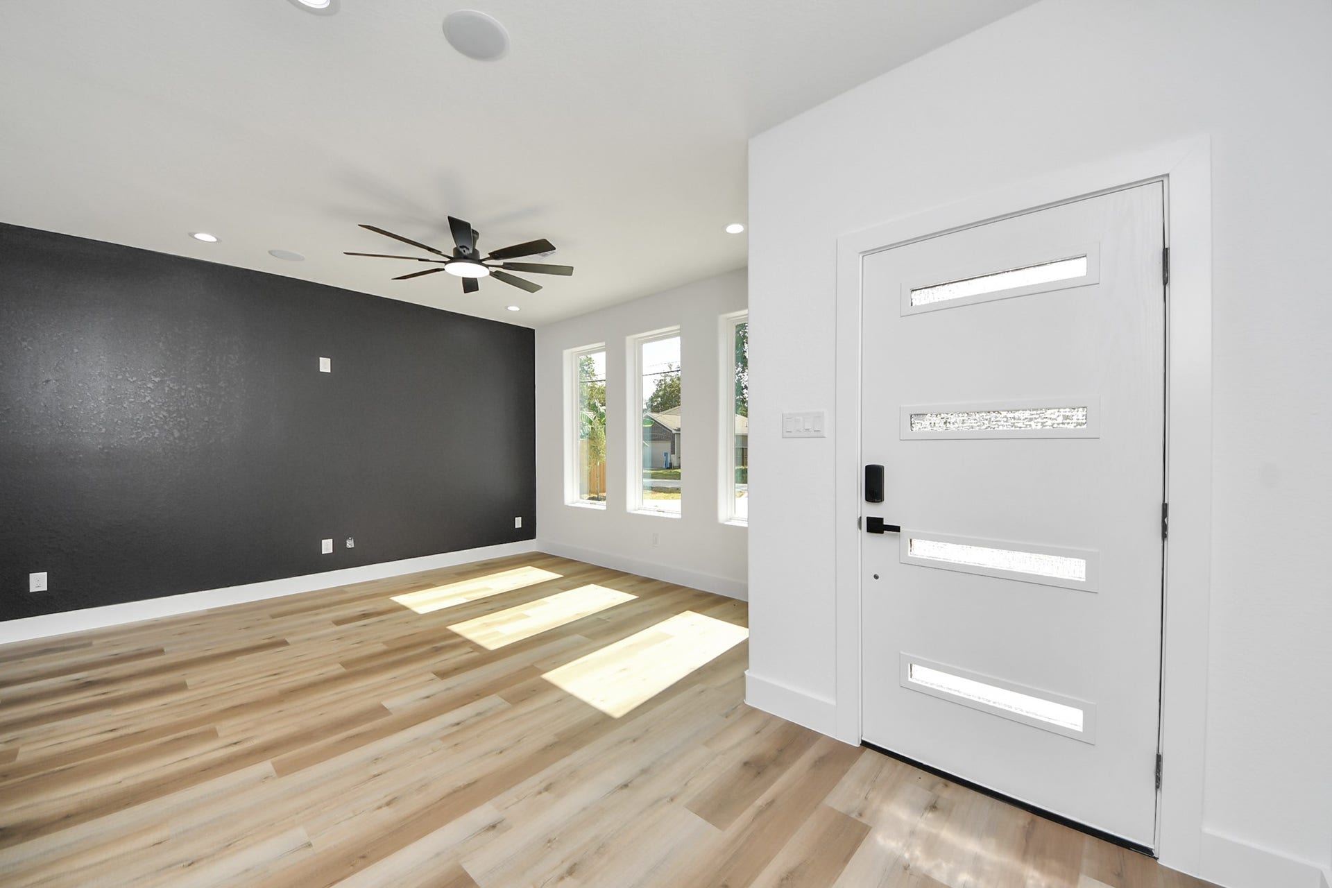 7801 King Street, Houston, TX 77028 Bright and modern entryway featuring a sleek front door, large windows, wood flooring, and a bold accent wall with a contemporary ceiling fan.