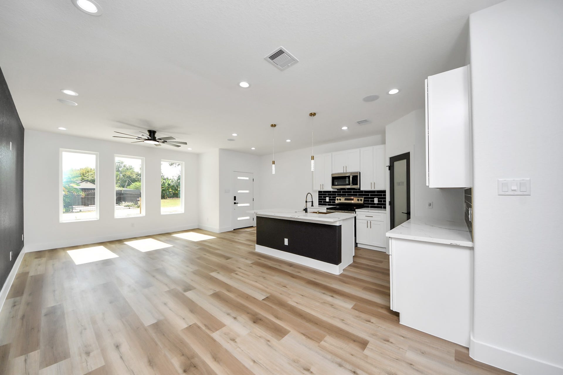 7801 King Street, Houston, TX 77028 Spacious open-concept living area with abundant natural light, featuring sleek wood flooring, a modern kitchen with a central island, and stylish black and white cabinetry.