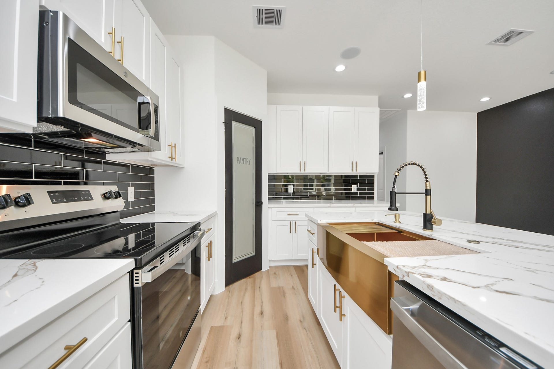 7801 King Street, Houston, TX 77028 Modern kitchen featuring sleek white cabinetry, stainless steel appliances, and elegant marble countertops. The black subway tile backsplash adds a touch of sophistication, complemented by a contemporary gold faucet and stylish pantry door.
