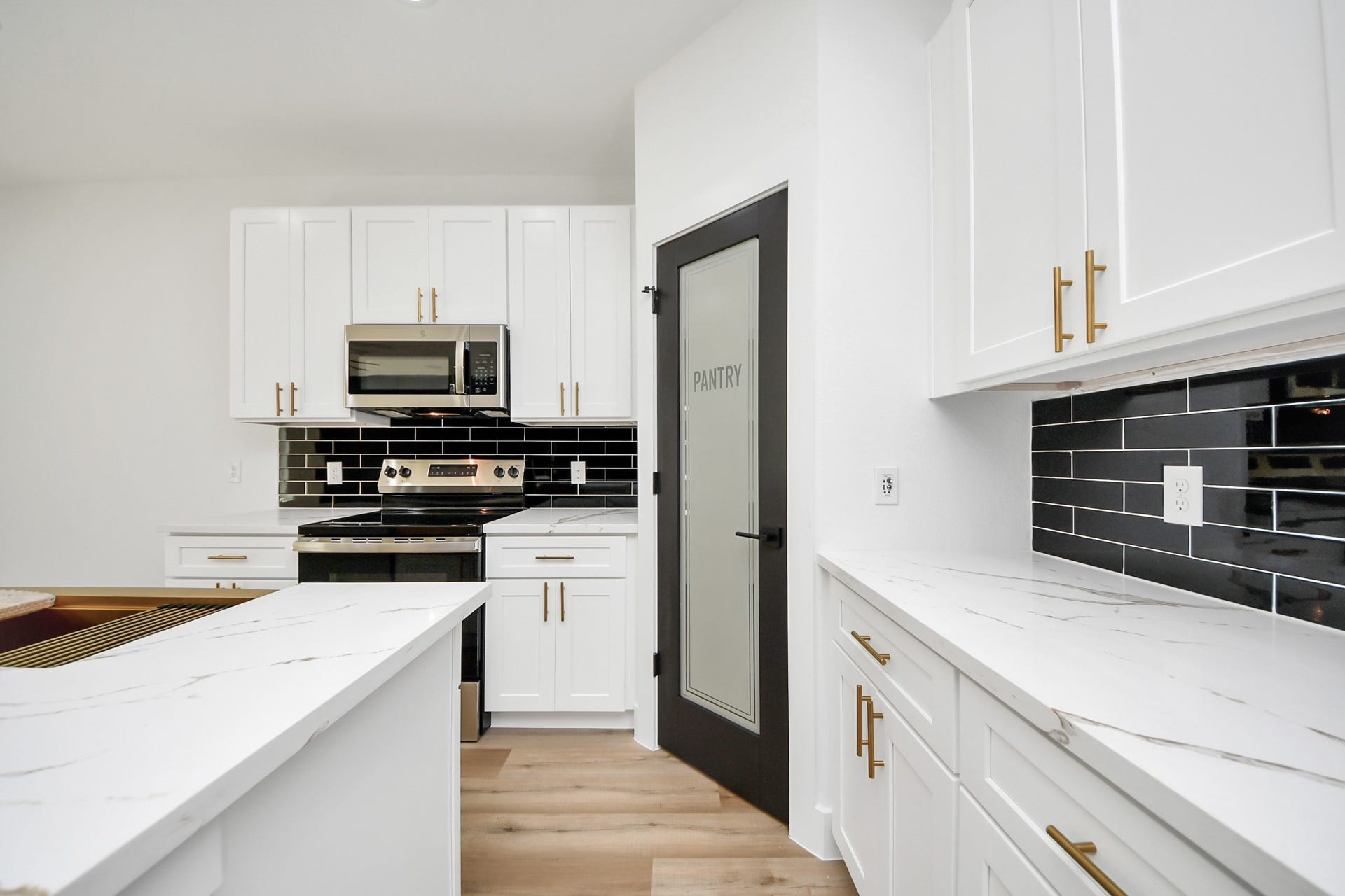 7801 King Street, Houston, TX 77028 Modern kitchen featuring sleek white cabinetry, elegant marble-style countertops, and a striking black tile backsplash. Equipped with stainless steel appliances and a convenient pantry with a frosted glass door.